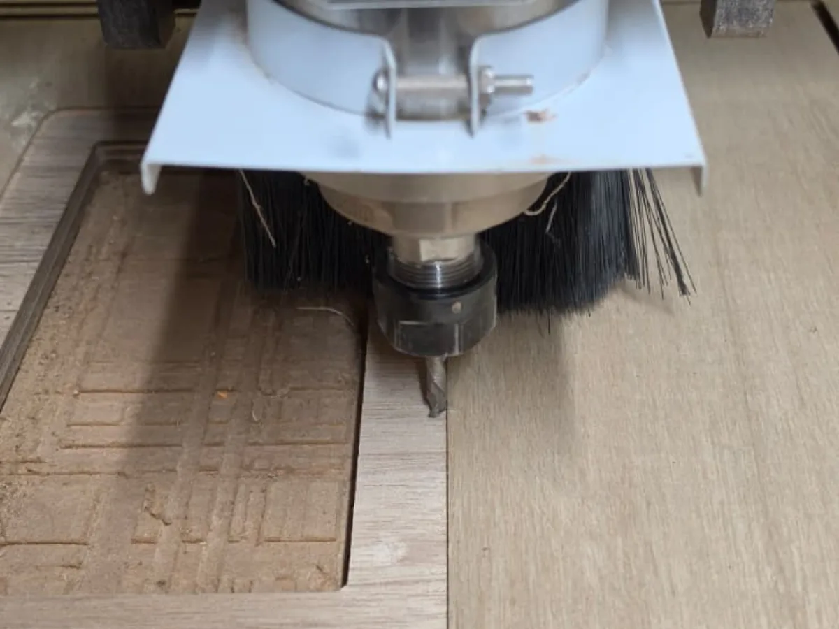 CNC router bit cutting a speaker cabinet panel out of a marine plywood sheet, with the dust extraction brush around the spindle
