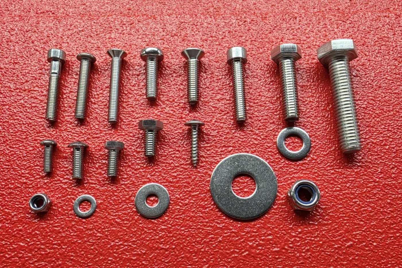 The full range of stainless steel bolts, screws, washers and nyloc nuts used in a Prime Audio cabinet, laid out on red textured coating