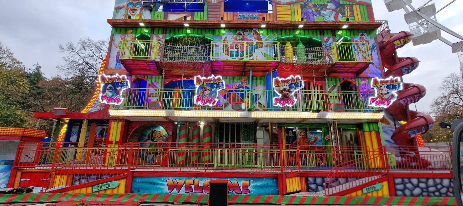Apres Ski Party fun house, a brightly painted multi-storey fairground attraction with a speaker cabinet at the entrance